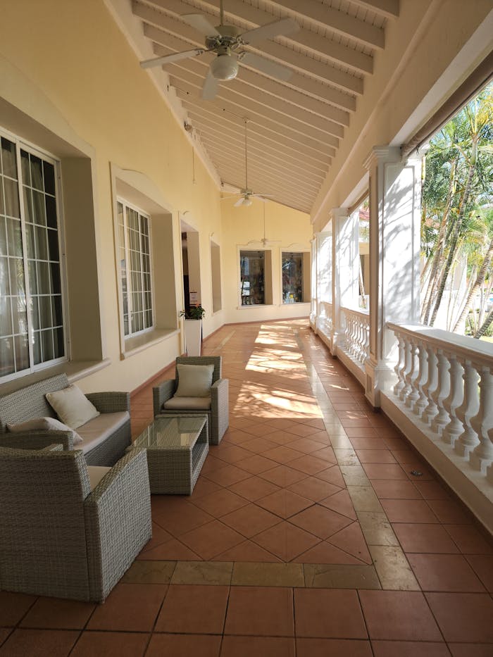 Bright and inviting terrace with wicker furniture, ceiling fans, and sunlit ambiance.