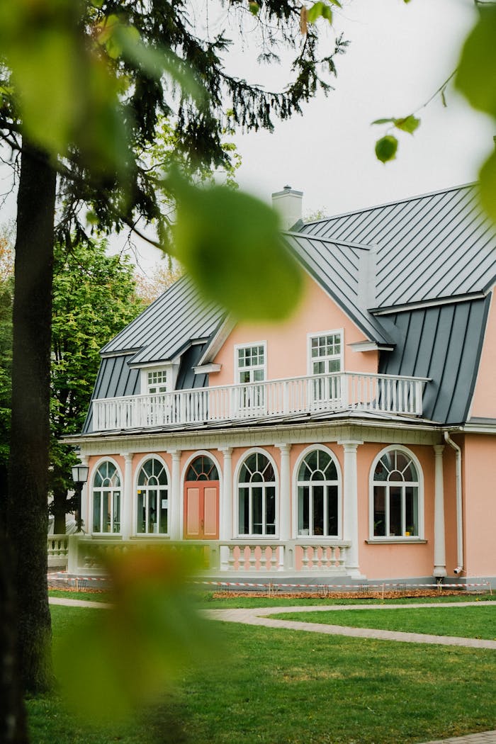 Elegantly designed pink house surrounded by lush greenery, showcasing classic architecture.